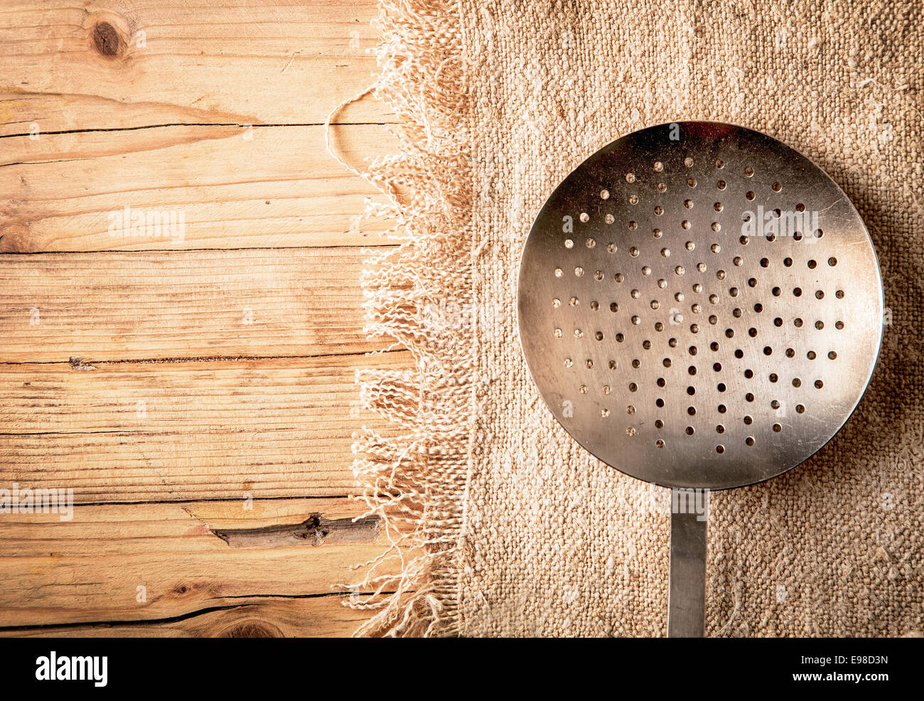 Ancienne passoire métallique circulaire, tamis ou tamis perforé avec trous pour essorer légumes tout en préparant un repas dans une cuisine de campagne sur un fond de bois texturés avec copyspace Banque D'Images