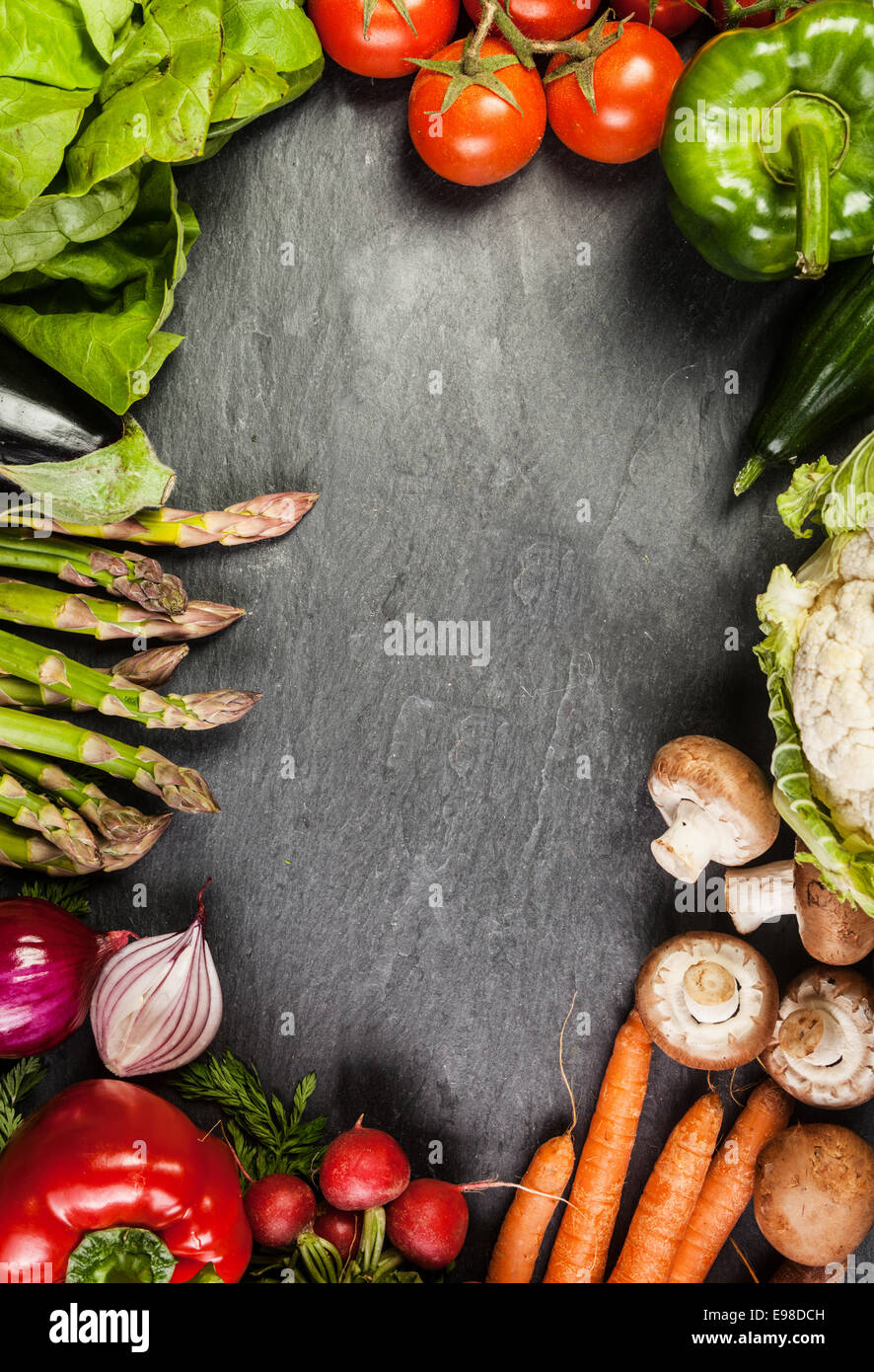Cadre ou une bordure d'un assortiment de légumes frais de la ferme sur ardoise avec copyspace y compris les carottes, asperges, tomate, poivron, carottes Banque D'Images