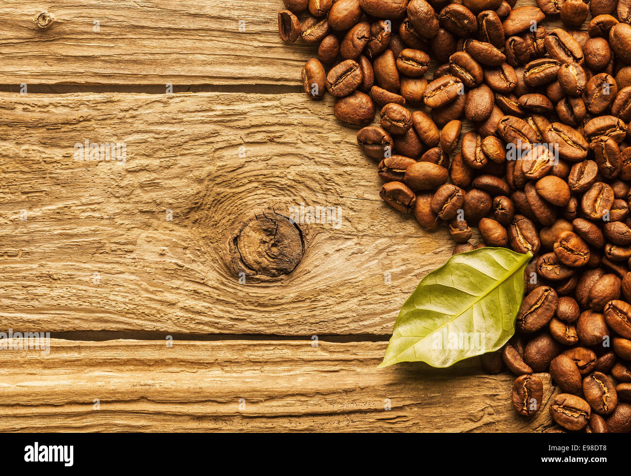 Tas de grains de café torréfié frais disposés comme une frontière d'angle sur les planches de bois rustique texturé avec un café vert feuille et copyspace Banque D'Images