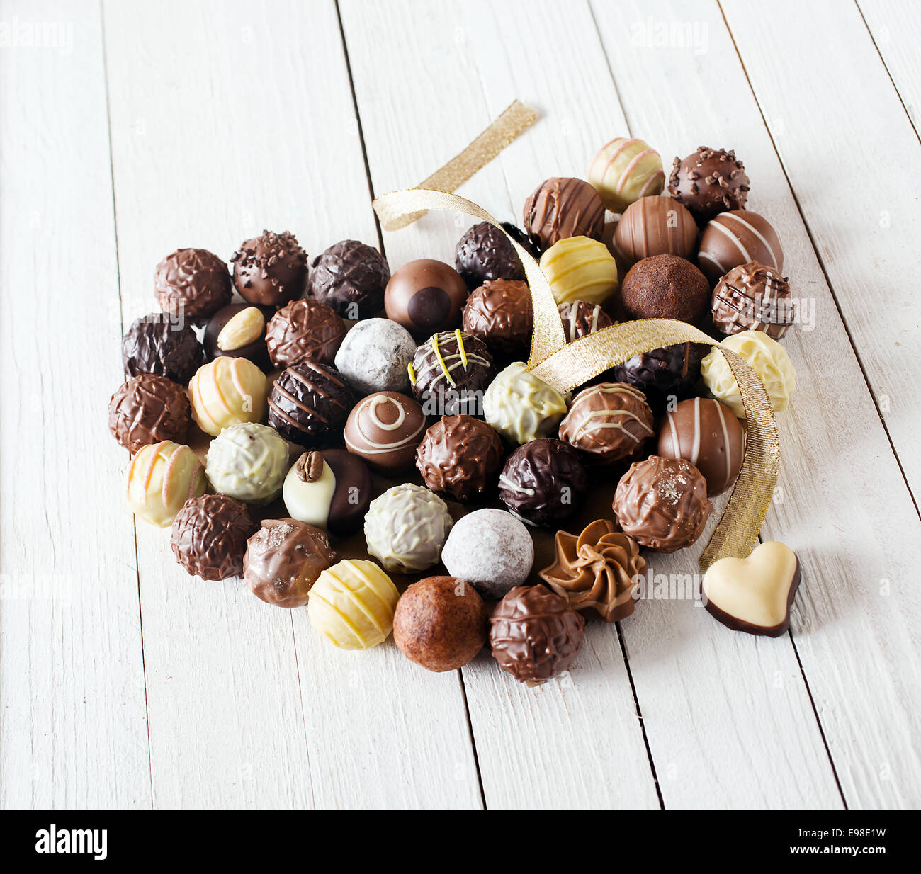 Close-up of a heart shape réalisés avec différents types de truffes au chocolat décoré d'un ruban d'or bouclés sur une table en bois blanc Banque D'Images