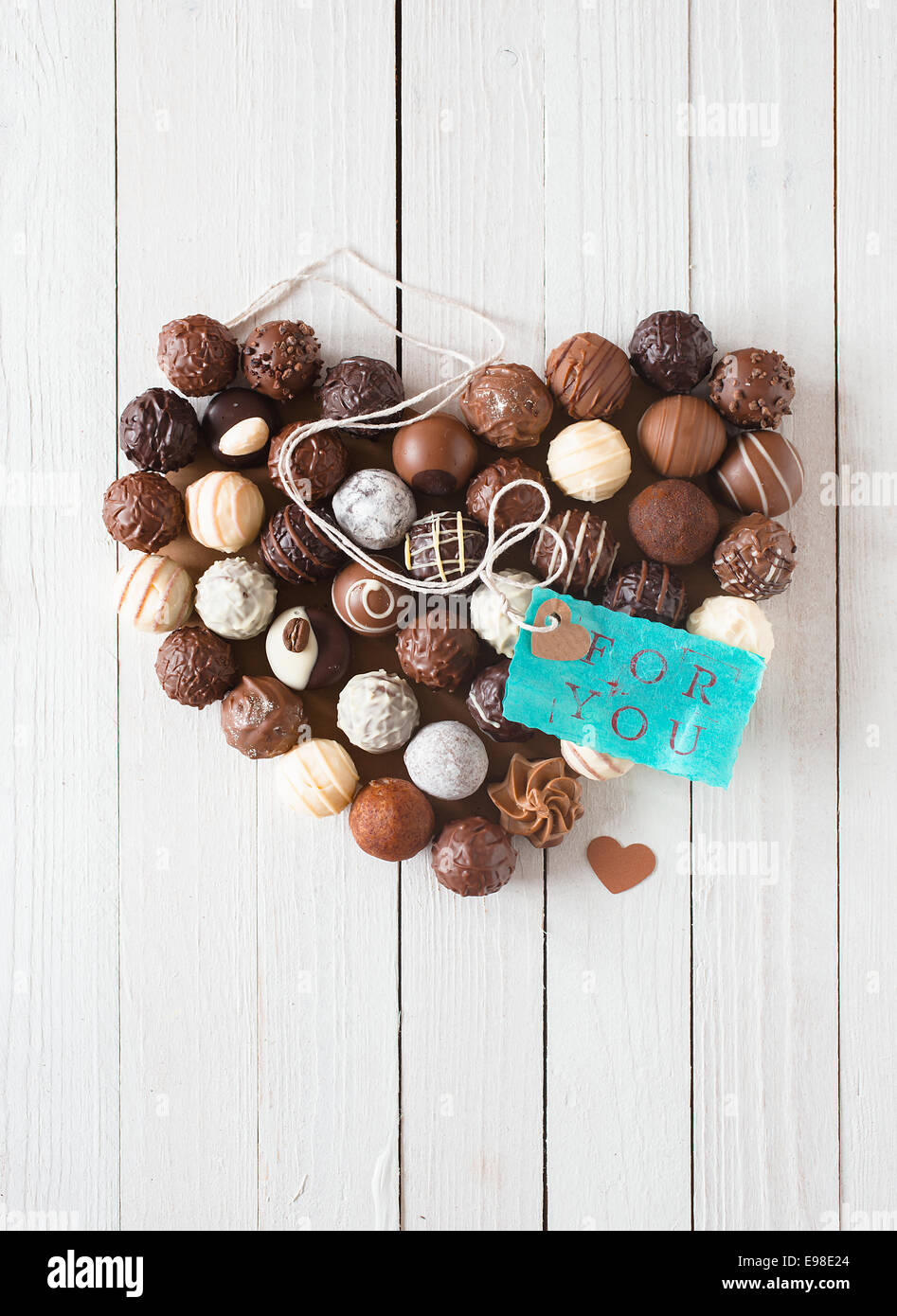 Forme de coeur fait avec divers types de truffes au chocolat et une étiquette bleue avec un message romantique sur une table en bois blanc Banque D'Images