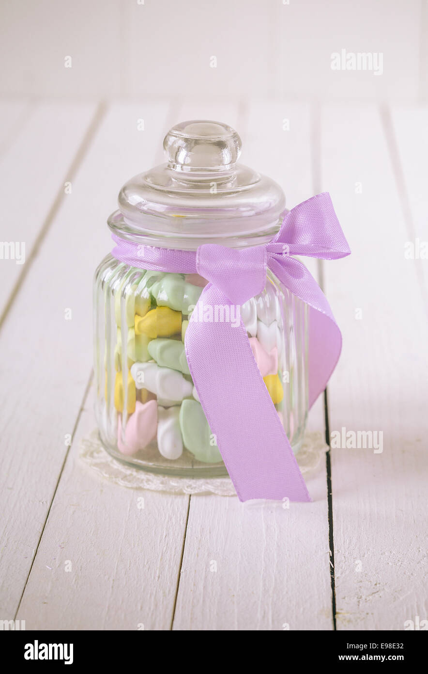 Verre ancien bocal rempli de bonbons colorés avec Sucre et amandes un arc violet sur un fond de bois blanc Banque D'Images