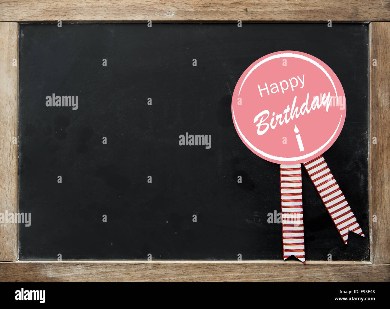 Joyeux anniversaire fête avec rosette rubans rayés sur un vintage kids school ardoise avec cadre en bois et une surface vide noir avec copyspace pour votre texte Banque D'Images