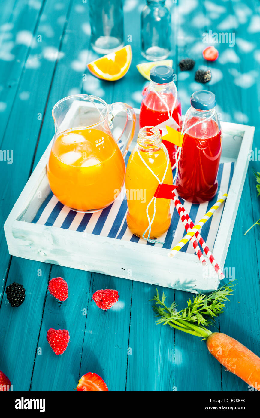 Bouteilles de jus d'agrumes et jus de fruits faits maison avec un pichet de jus d'orange et de carotte glacé servi mélange sur un en bois Banque D'Images