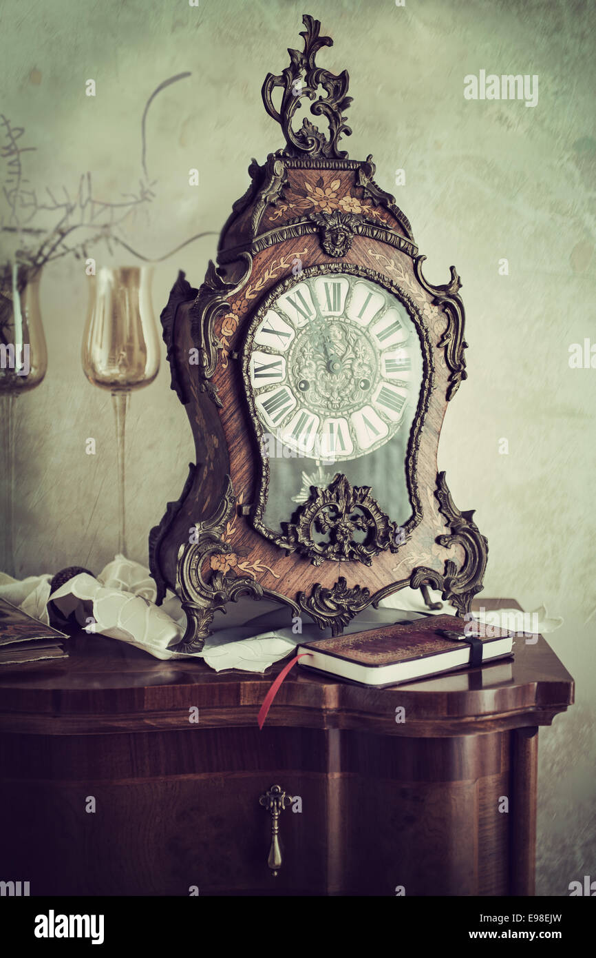 Manteau ornés d'horloge avec un cas incrusté dans le style baroque et cadran fantaisie sur le dessus d'une commode avec un journal ou une revue dans un concept de gestion du temps Banque D'Images