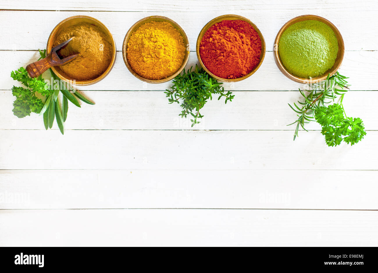 Les herbes culinaires et les épices colorés dans des bols en bois debout dans une ligne blanche sur les panneaux peints avec copyspace ci-dessous, overhead view Banque D'Images