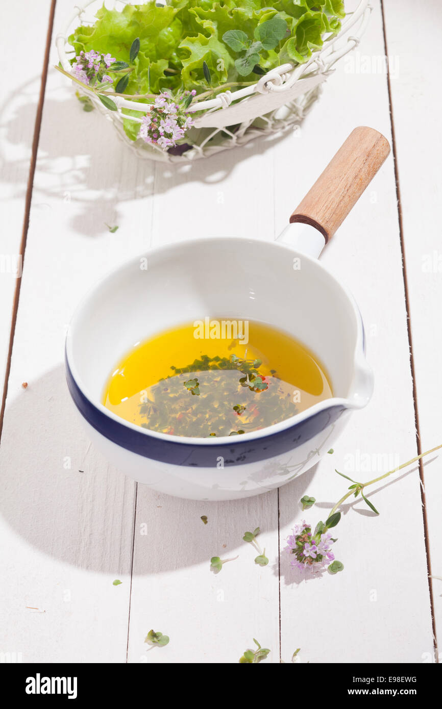 Plat de céramique de golden l'huile d'olive et vinaigrette aux herbes fraîches hachées sur un comptoir de cuisine en bois blanc avec un bol de coriandre Banque D'Images