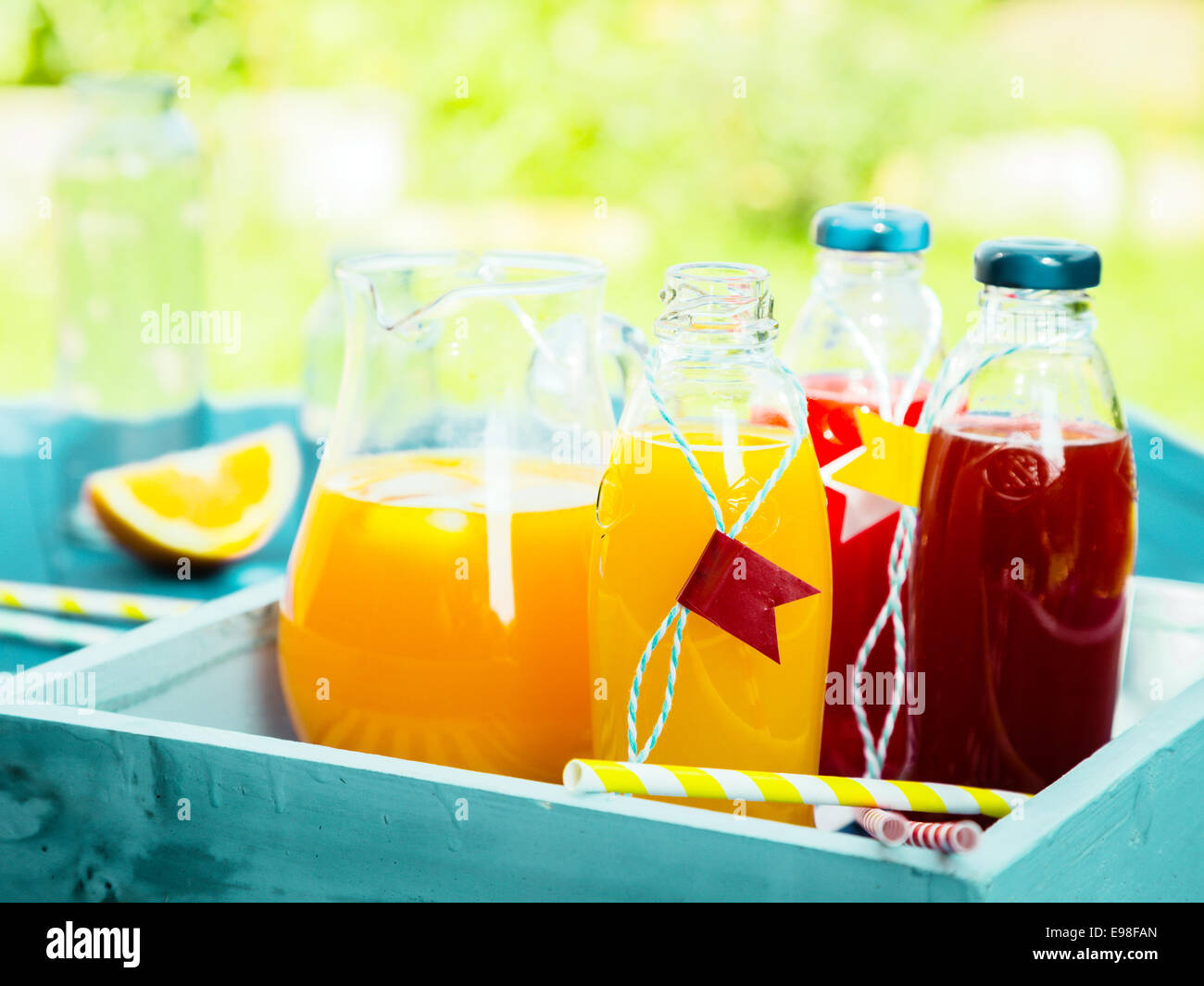 Des jus de fruits fraîchement pressés avec des bouteilles de mélange d'agrumes orange et jus de fruits frais sur une table de pique-nique turquoise dans un jardin d'été Banque D'Images