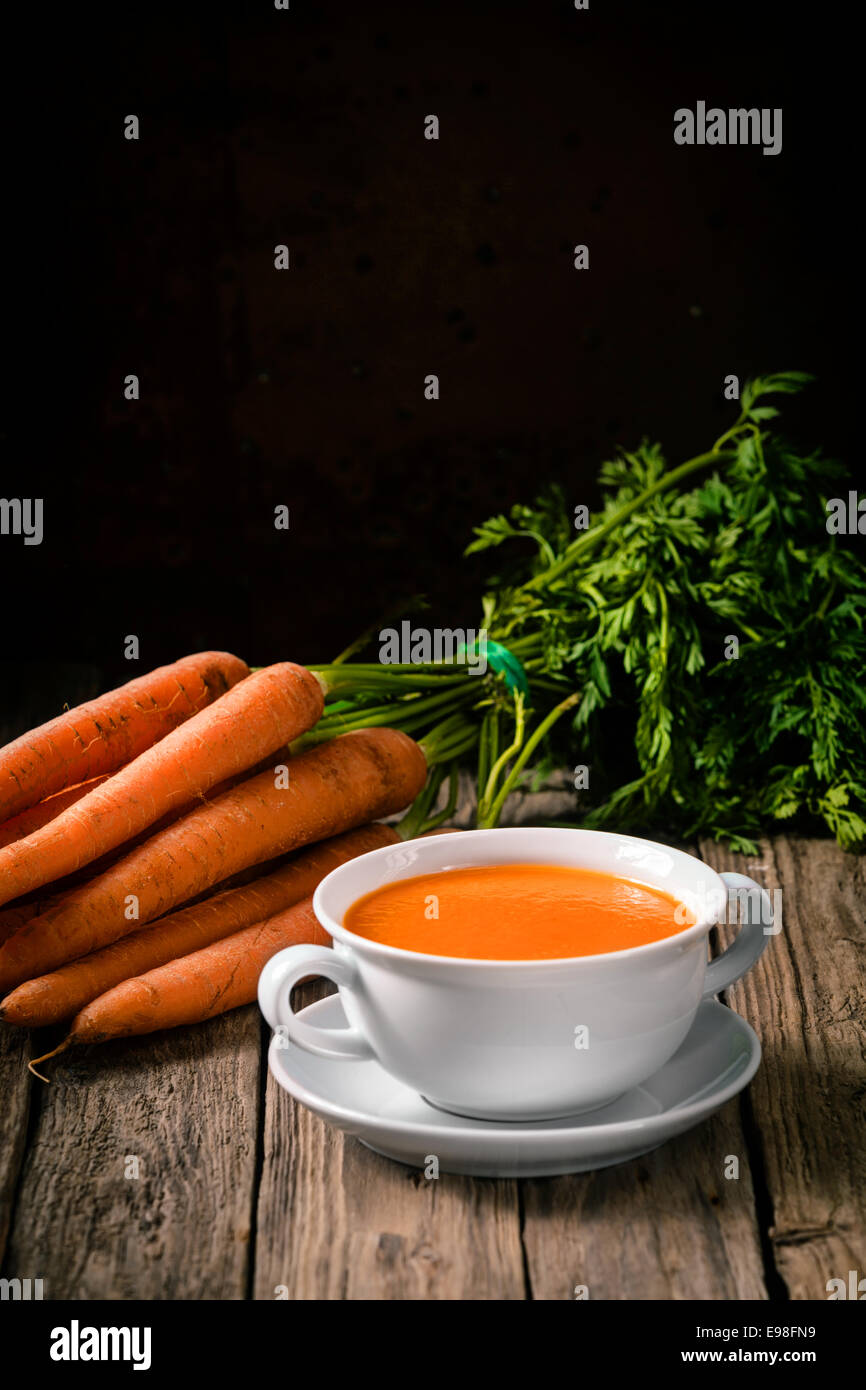 Bol de soupe de carottes chaud maison délicieux avec des ingrédients frais sur un comptoir de cuisine en bois rustique avec copyspace Banque D'Images