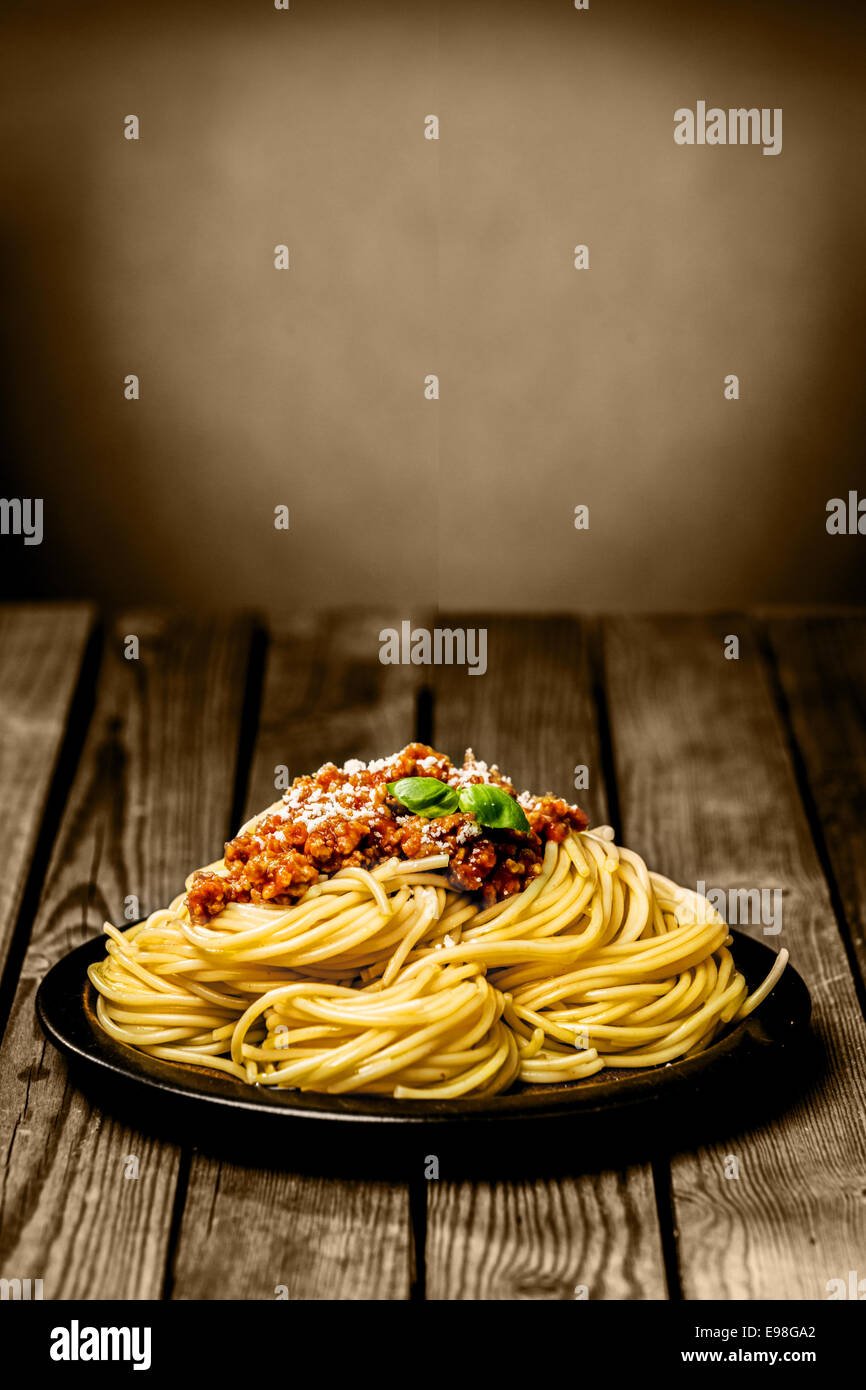 Assiette de spaghetti Bolognese italien surmontée avec du boeuf haché et du basilic et saupoudré de parmesan sur une table en bois rustique avec copyspace Banque D'Images