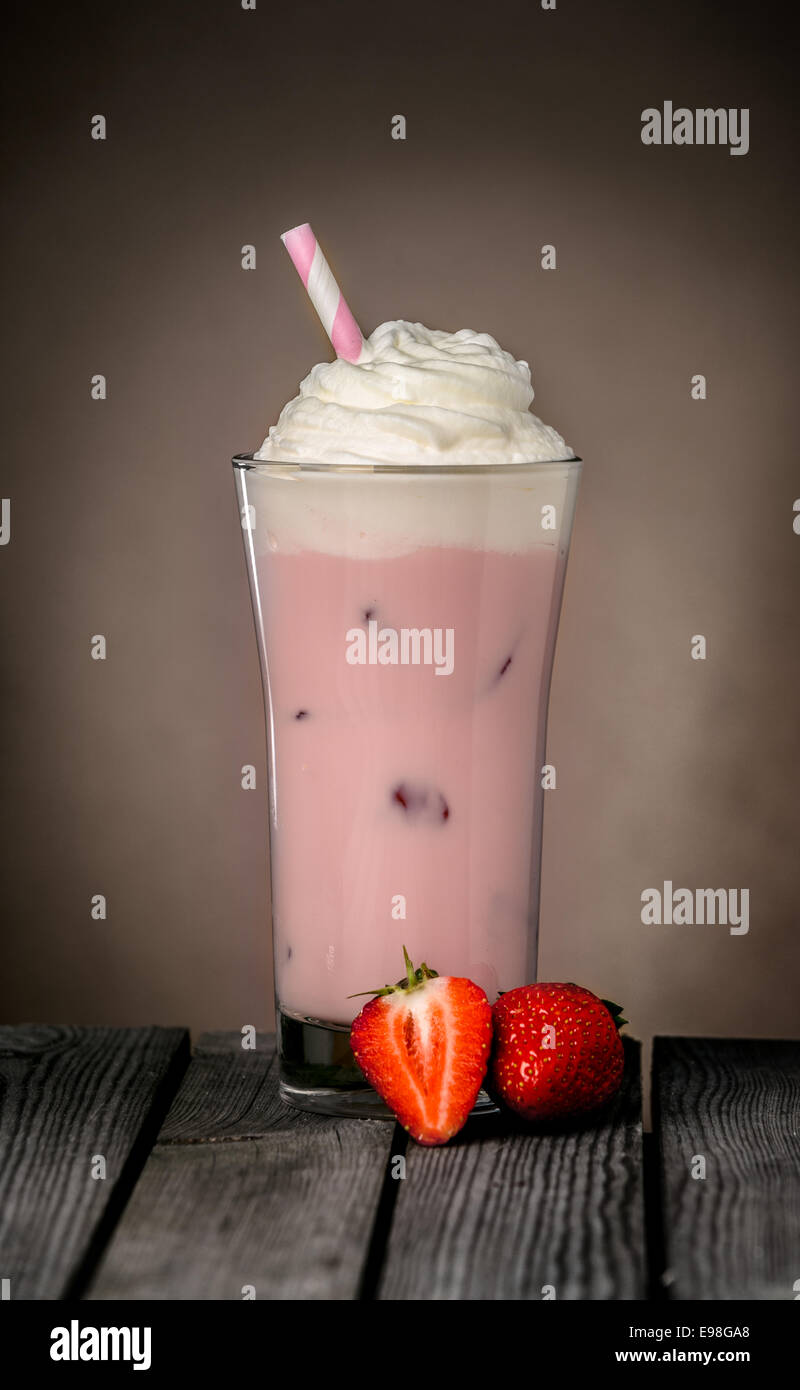 De délicieux milk-shake aux fraises froide rafraîchissante avec des fraises fraîches garnies de crème glacée ou de la crème glacée et servi dans un grand verre sur une table en bois rustique Banque D'Images