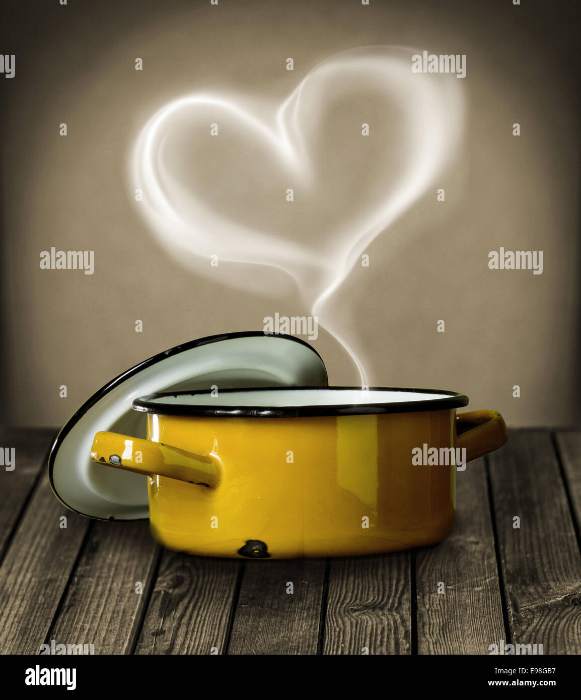 La vapeur en forme de coeur planant dans l'air au-dessus d'une marmite en métal émaillé jaune symbolique de l'amour sur un comptoir de cuisine en bois rustique Banque D'Images