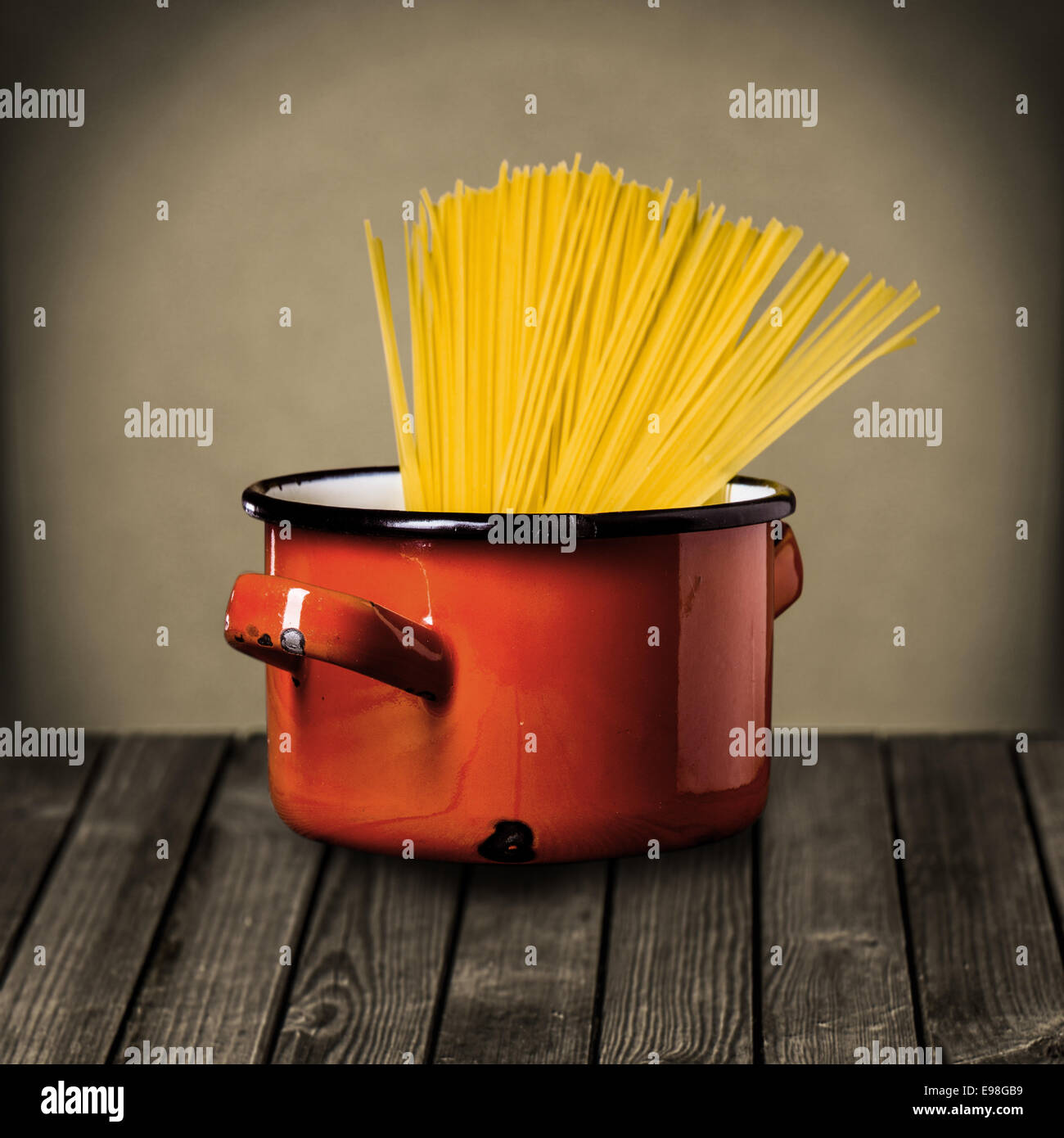 Spaghetti italien non cuits dans un pot émaillé rouge debout sur un comptoir de cuisine en bois rustique, tout en préparant un délicieux repas de pâtes italiennes Banque D'Images