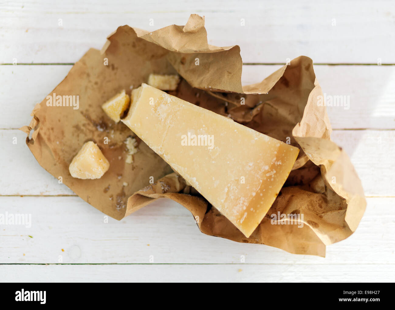 Coin de fromage parmigiano-reggiano granulaire dur largement utilisé dans la cuisine italienne dans une enveloppe de papier brun sur les tableaux blancs vu de passage Banque D'Images