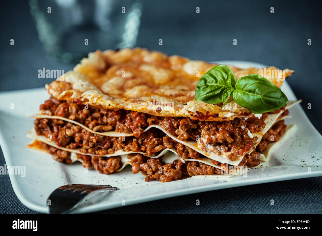 Lasagne au boeuf italien épicé boeuf assaisonné et tomates entre des feuilles de nouilles aux œufs garnie de fromage grillés et de basilic frais sur une plaque blanche moderne Banque D'Images