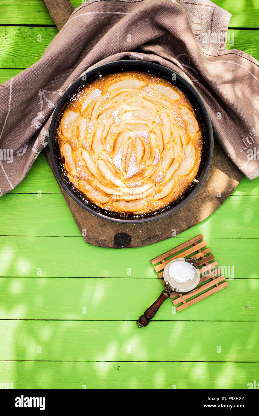 Fresh home pomme au four tarte dans un plat à four avec une petite passoire avec du sucre en poudre pour saupoudrer sur le dessus sur une table de jardin vert Banque D'Images