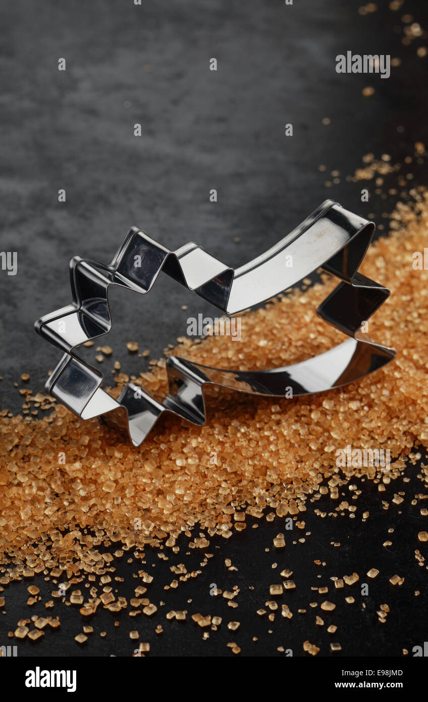 Shooting Star aluminium brillant de coupeur de biscuit de Noël sur un lit de cristaux de sucre brun caramélisé sur un fond sombre avec copyspace pour vos souhaits de saison Banque D'Images