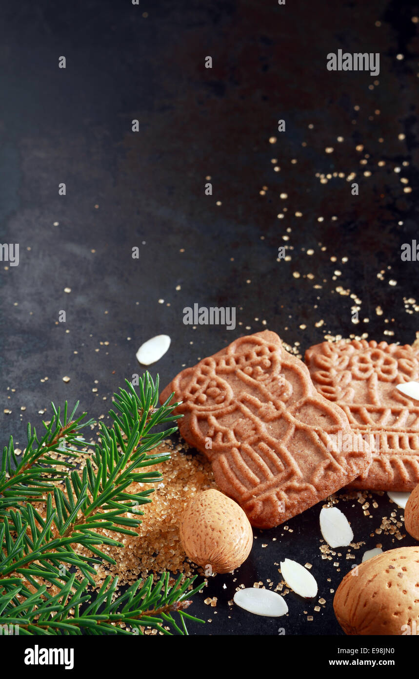 Croquant spéculoos épicés traditionnels de Noël à l'origine néerlandais buscuits au four pour la fête de Saint Nicolas avec amandes et flocons et une branche de pin, sur une sombre backgorund avec copyspace Banque D'Images