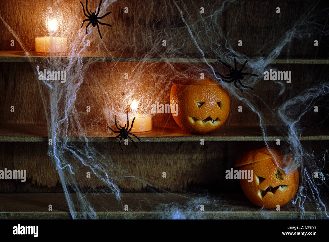Deux Halloween Jack o lanterne sculptée à partir d'Oranges et d'araignées avec des araignées et allumé des bougies sur des étagères Banque D'Images