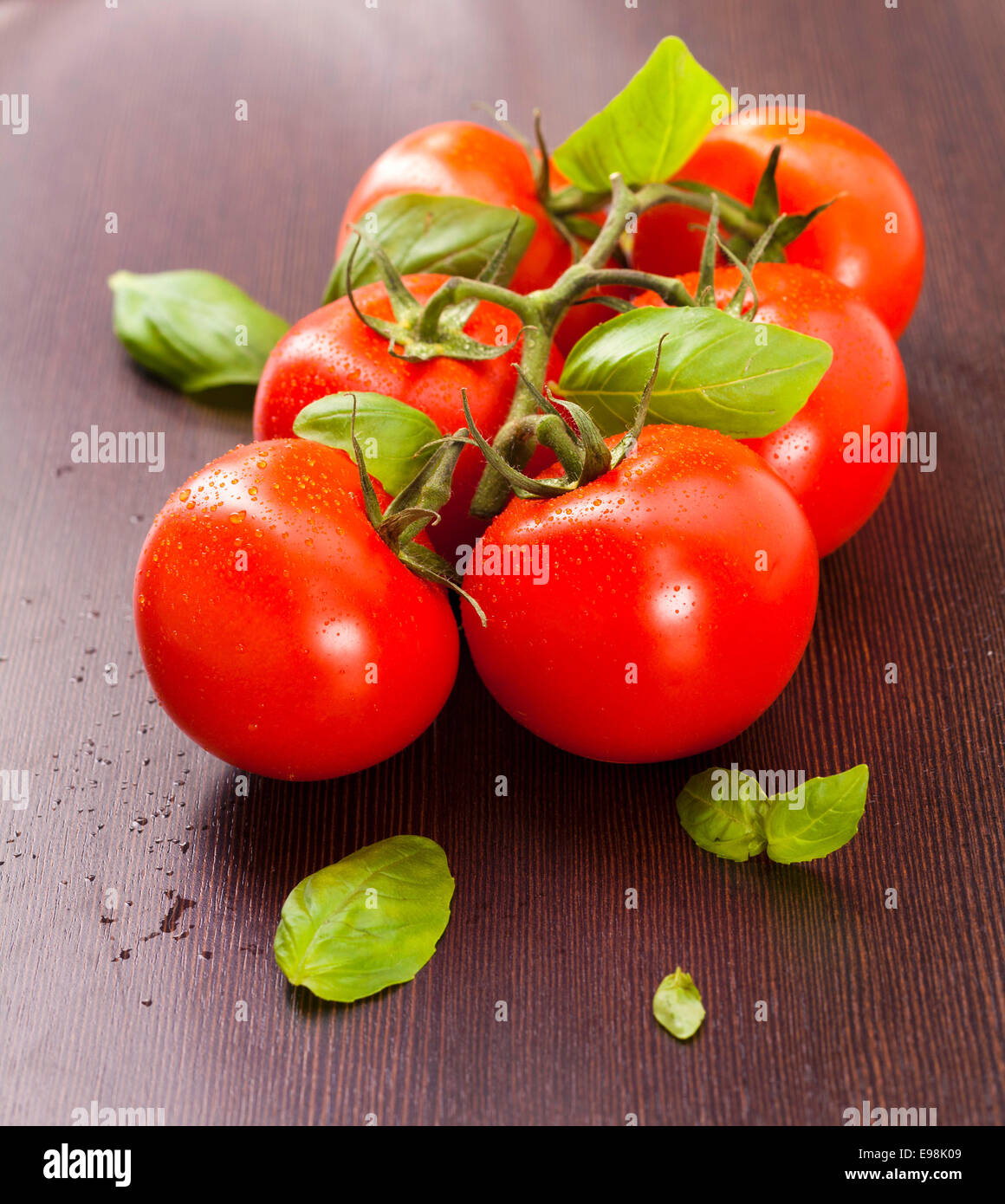 Les tomates mûries sur pied de basilic sur une plaque de bois Banque D'Images