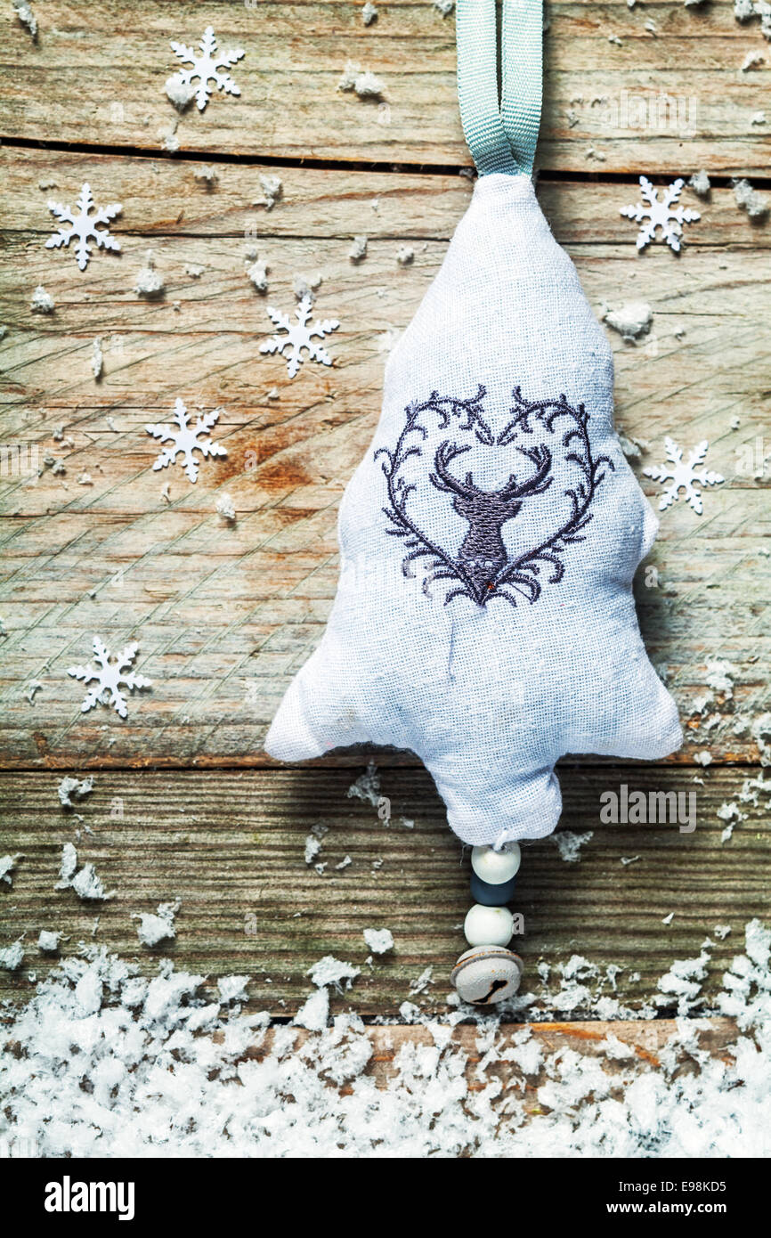 Textiles brodés à la main décoration d'arbre de Noël avec un renne et grelot suspendu à un cadre rustique en bois avec fond texturé et flocons de neige de l'hiver Banque D'Images