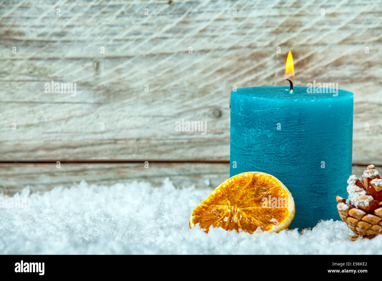 Blue Christmas candle burning colorés en hiver neige avec un cône de pin et de tranche d'orange séchée contre les planches de bois texturés avec copyspace pour votre message d'accueil Banque D'Images