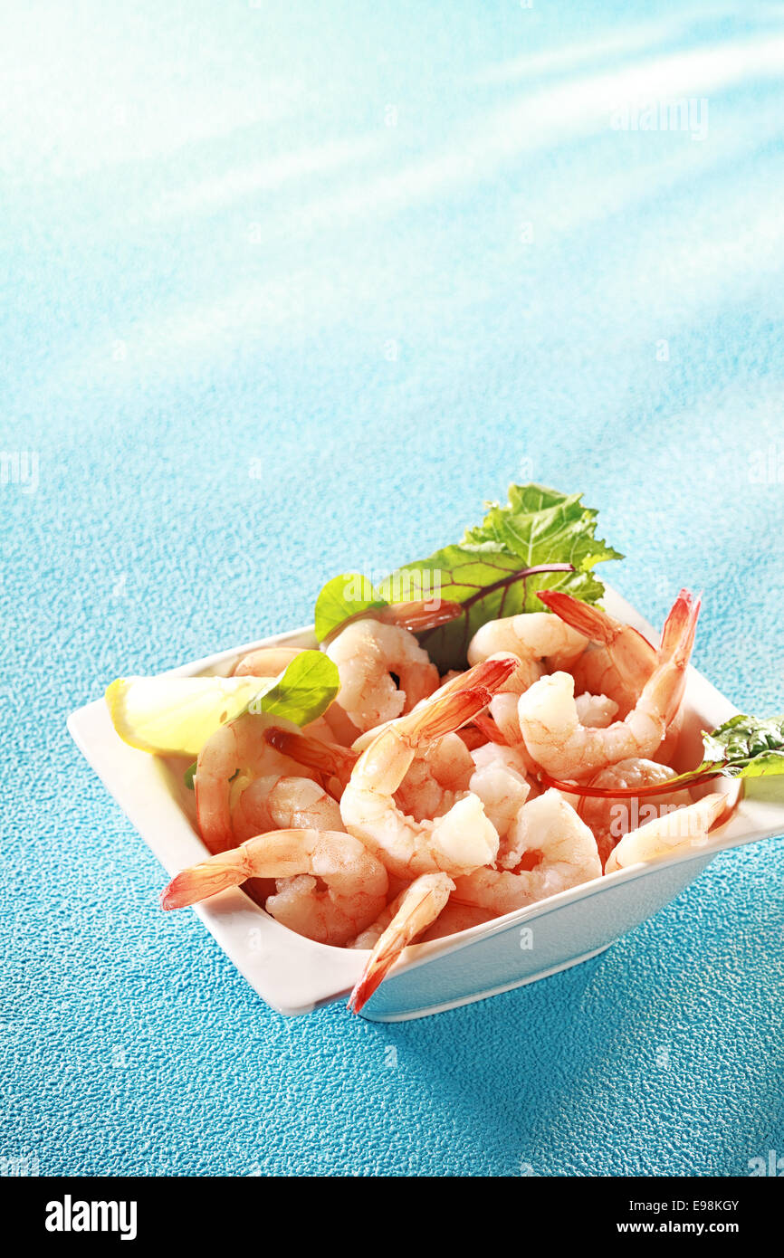 Crevettes crevettes roses fraîches ou apéritif servi avec des tranches de citron et les légumes verts pour une étape gourmande à un repas de début de coquillages, sur bleu Banque D'Images