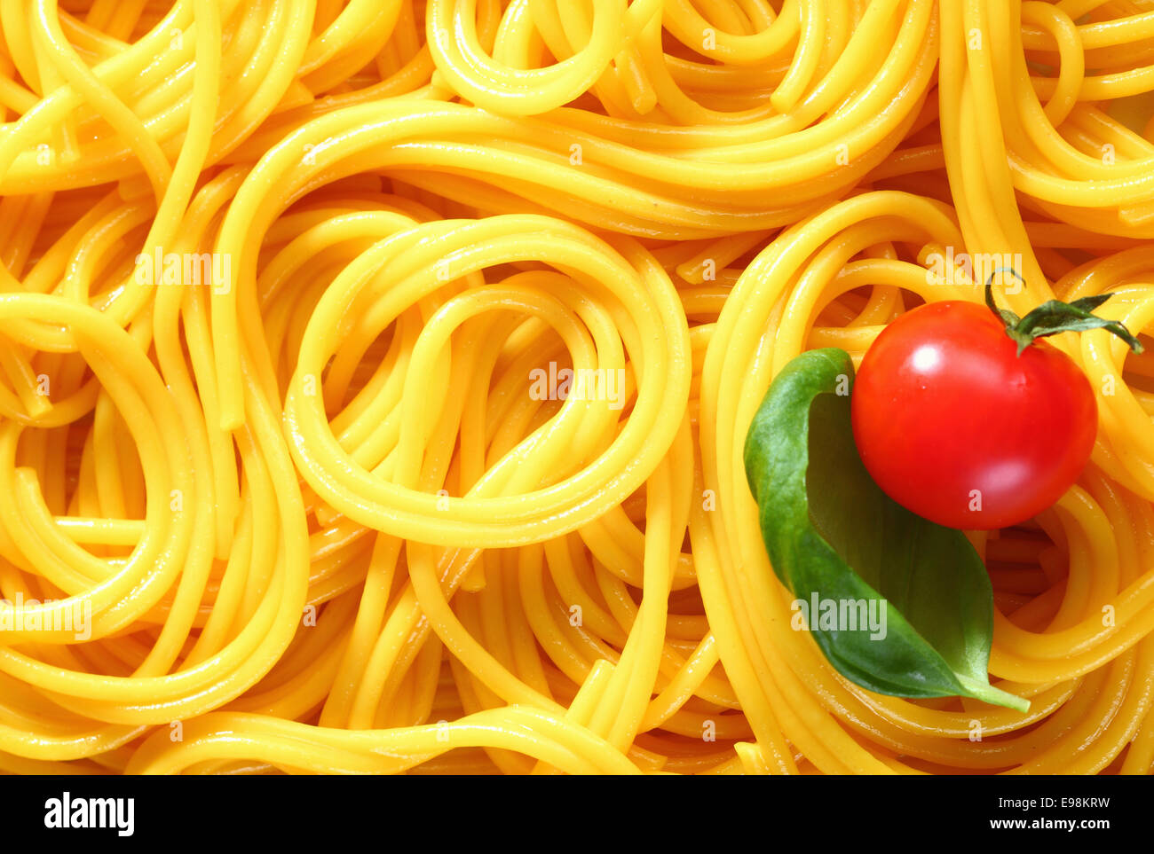 Gros plan du spaghetti fraîchement bouillie lovés dans des motifs aléatoires pour un arrière-plan intéressant. Avec le basilic et tomate Banque D'Images