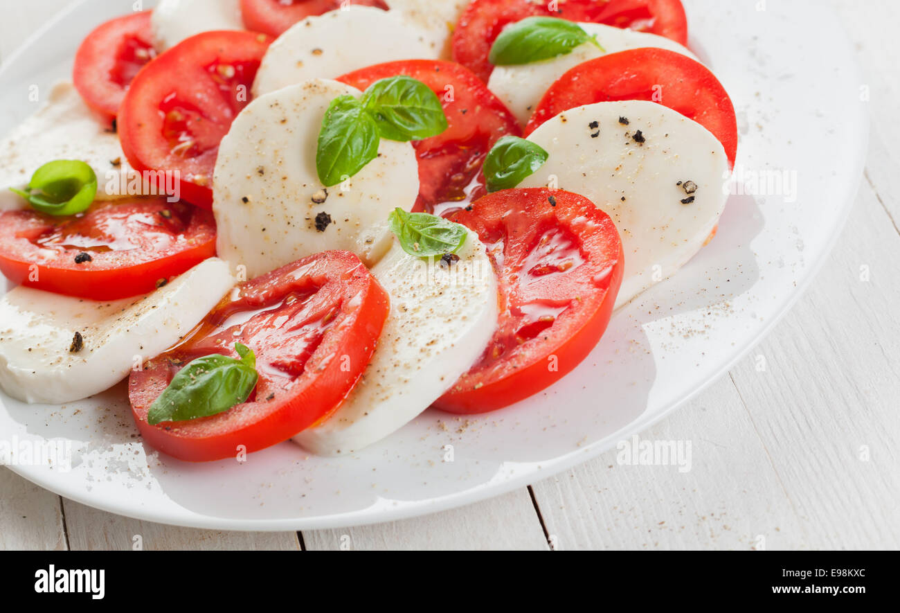 L'Italien tomate et mozzarella salade caprese assaisonné de sel et poivre et garnir de feuilles de basilic frais sur une plaque blanche Banque D'Images