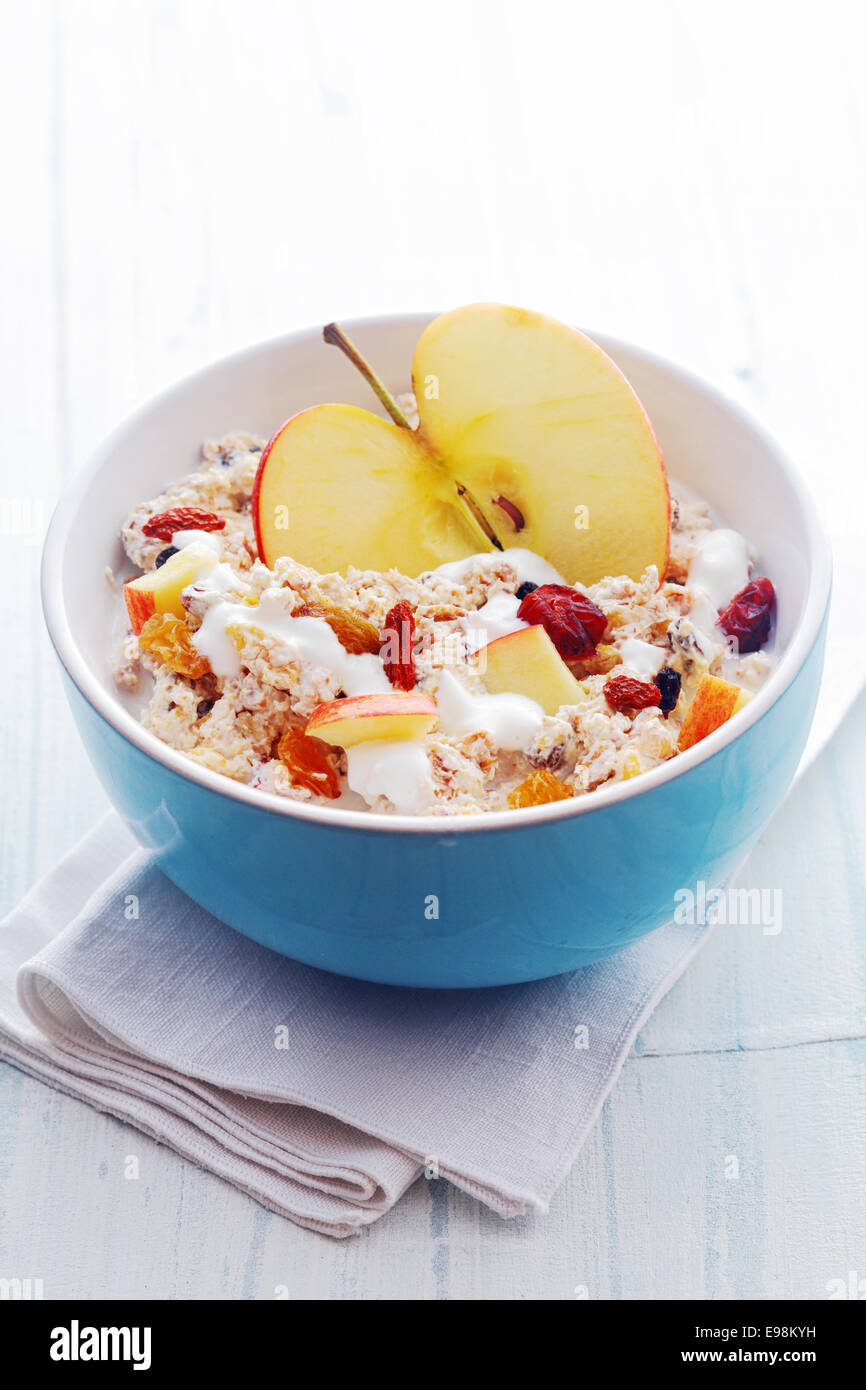 Bol de céréales du petit déjeuner sain avec une moitié de pomme fraîche et surmontée de dés de pomme, fruits secs et noix servi avec du lait dans un bol en céramique bleu, high angle view Banque D'Images