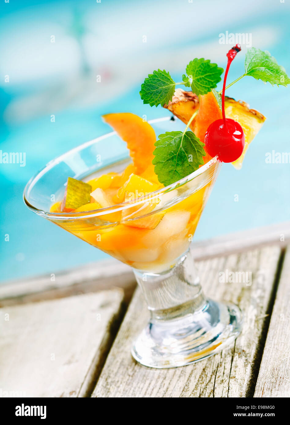 Cocktail de fruits tropicaux colorés rafraîchissante apéritif dans un verre conique rempli de morceaux de fruits frais sur la terrasse à côté d'une piscine bleu Banque D'Images