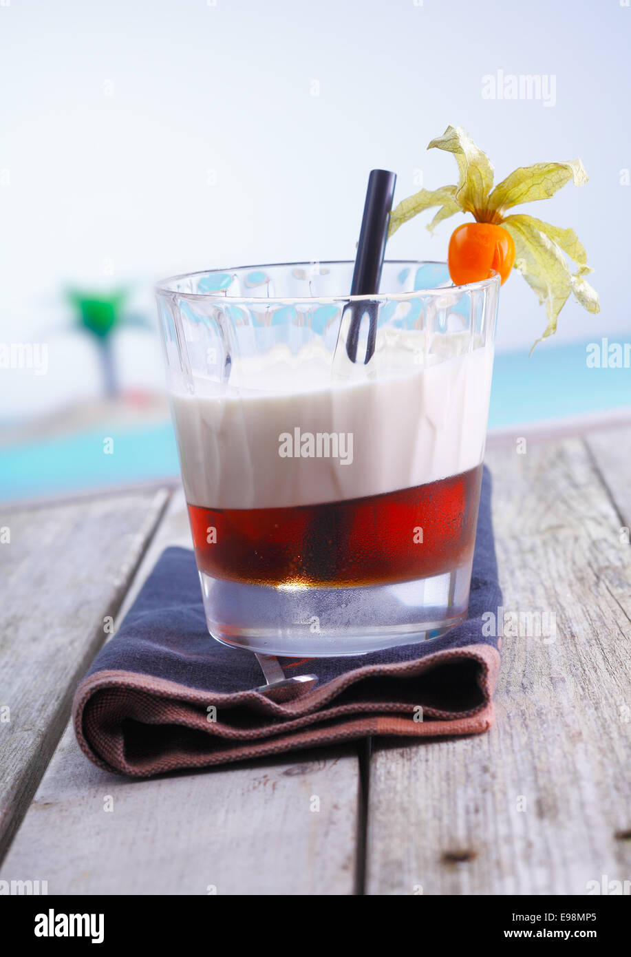 Cocktail sans alcool en couches avec garniture groseille servi sur une terrasse en bois par la mer Banque D'Images
