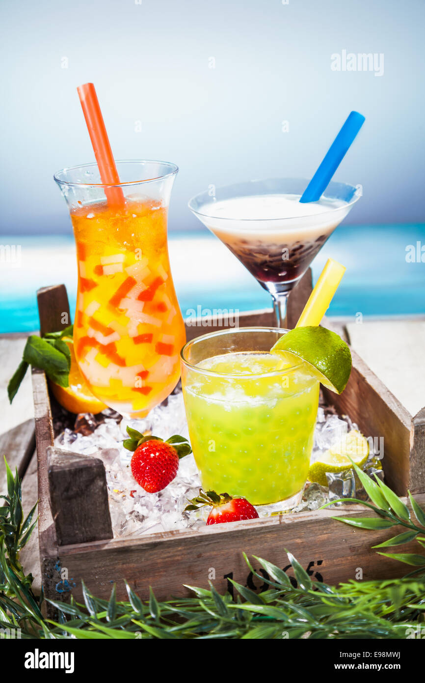 Trio de cocktails tropicaux colorés mélangés avec des fruits en forme de différents verres servis donnant sur une plage tropicale Banque D'Images
