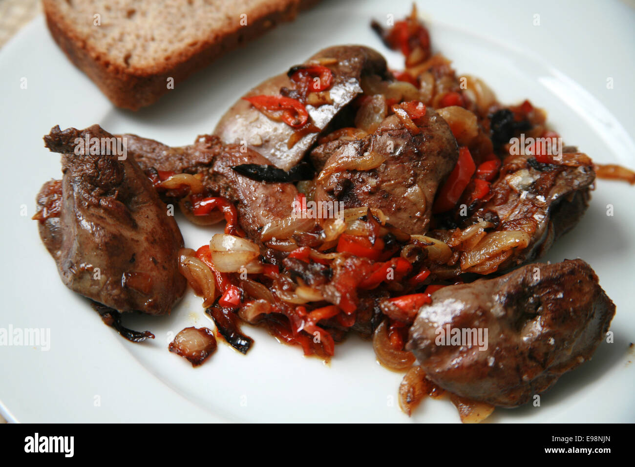 Foies de poulet frit avec des oignons et poivrons rouges caramélisés servi sur plaque blanche avec Brown et le pain de seigle et de basilic Banque D'Images