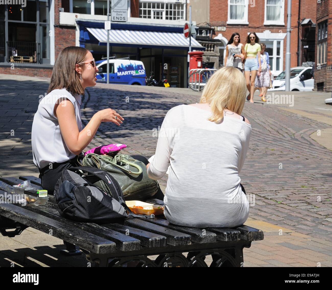 Deux jeunes femmes assises sur un banc en train de déjeuner le long de la route du château dans le centre-ville, Castle Road, Nottingham, Angleterre, Royaume-Uni. Banque D'Images