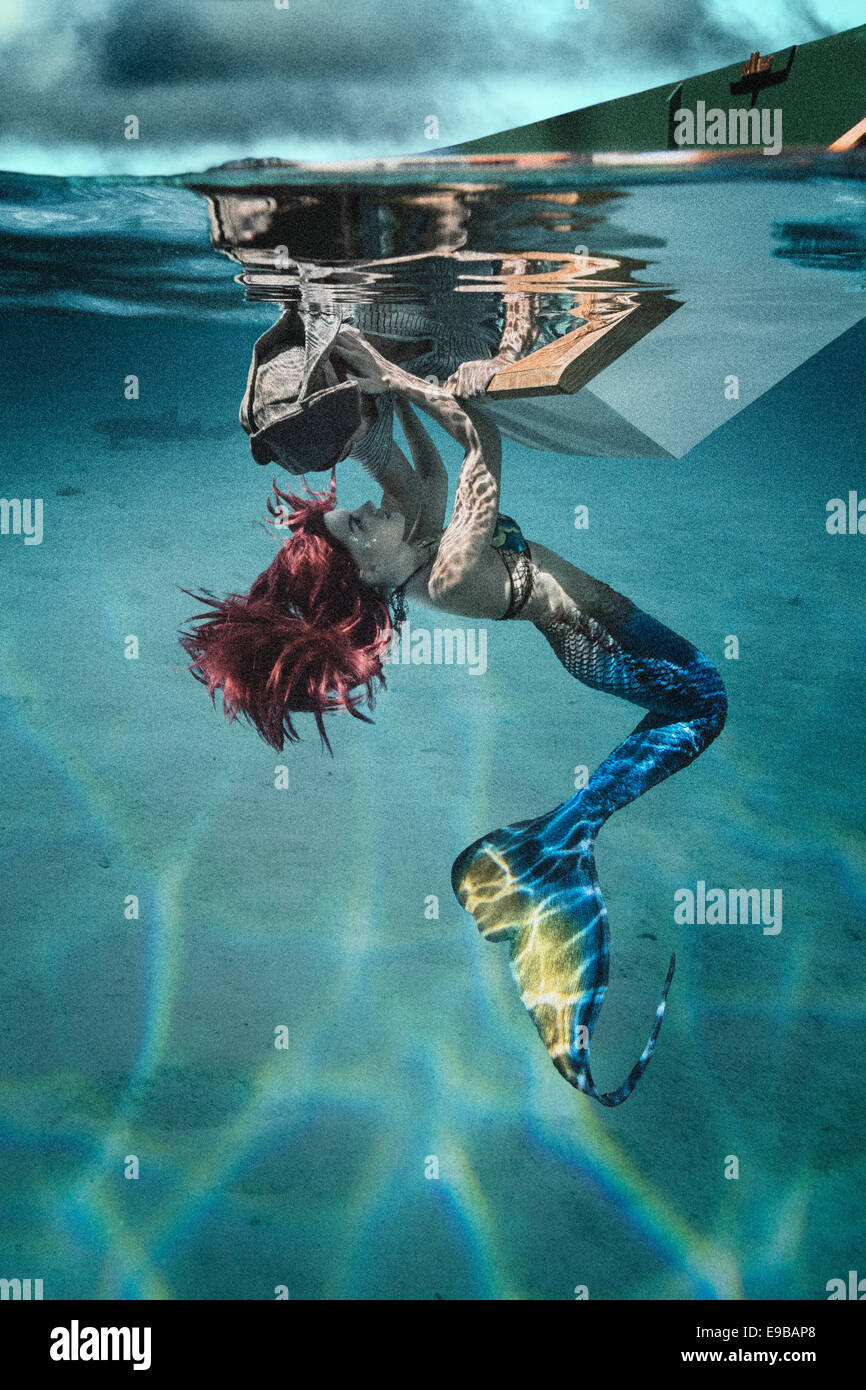 Sirène rousse tirant un petit bateau de pirate leurre sous l'eau par lui avec un baiser Banque D'Images
