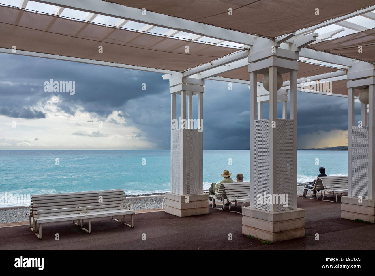 Couple de personnes âgées assis sur un banc à la promenade et regarder les nuages sombres, la pluie menaçante au dessus de la Méditerranée à Nice, France Banque D'Images