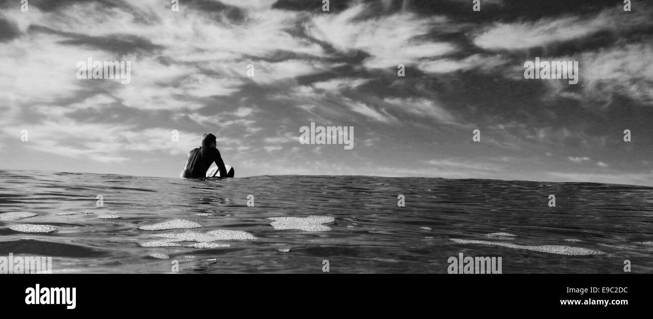 Guy Surfer en attente d'une vague dans l'océan en noir et blanc Banque D'Images