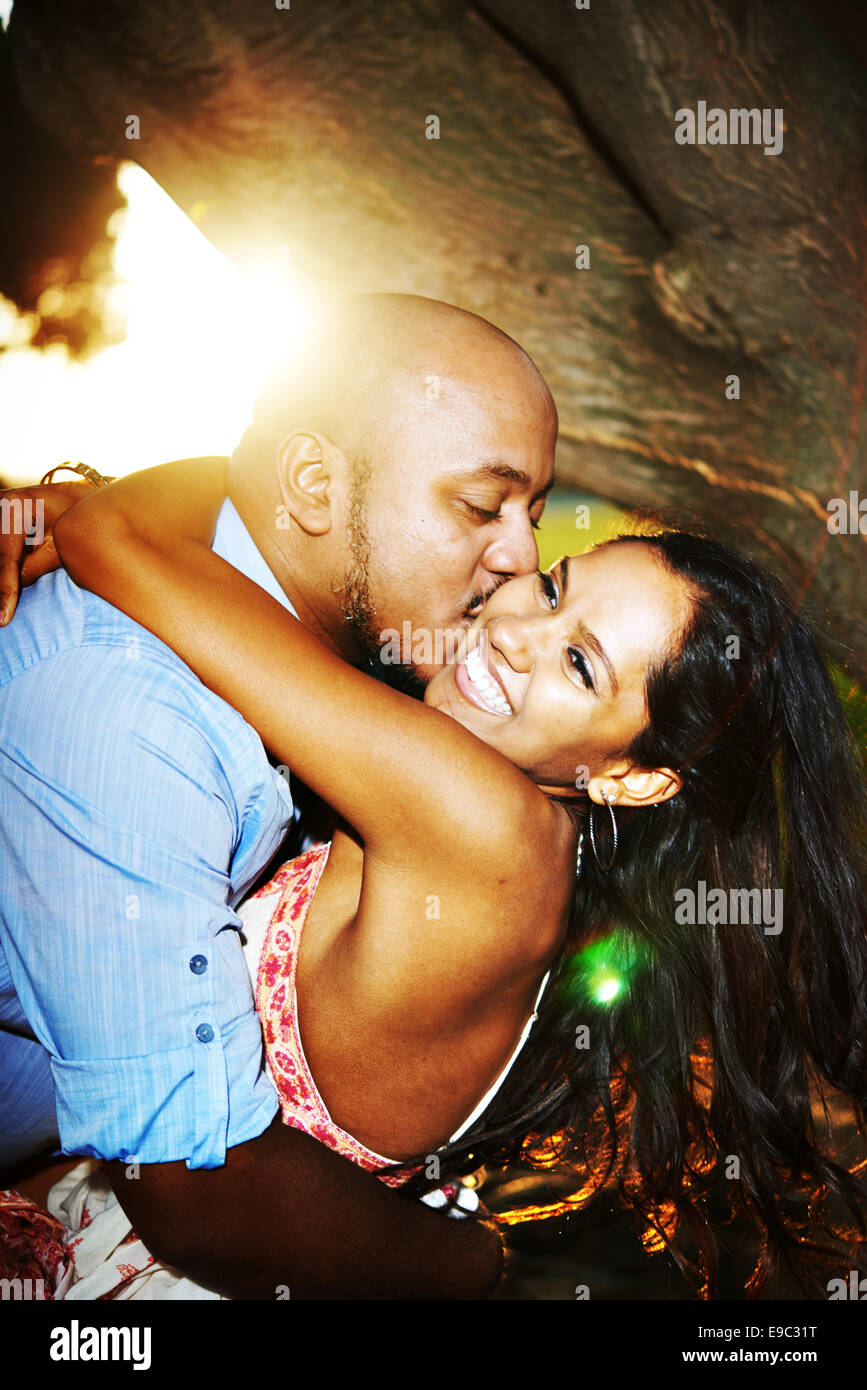 Couple pendant le coucher du soleil par arbre et souriant et serrant Banque D'Images