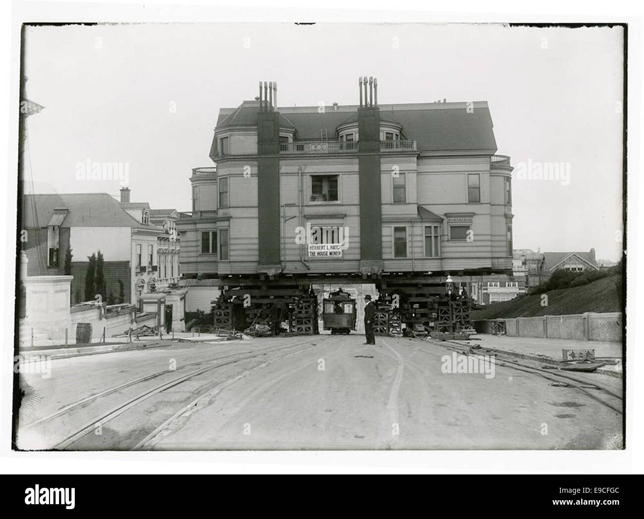 Cette image montre un téléphérique passant sous l'ancienne résidence de Claus Spreckels, un homme d'affaires de premier plan, alors qu'il est déplacé par Herbert L. Hatch, connu sous le nom de « The House Mover ». La scène capture un moment de l'histoire architecturale à San Francisco. Banque D'Images