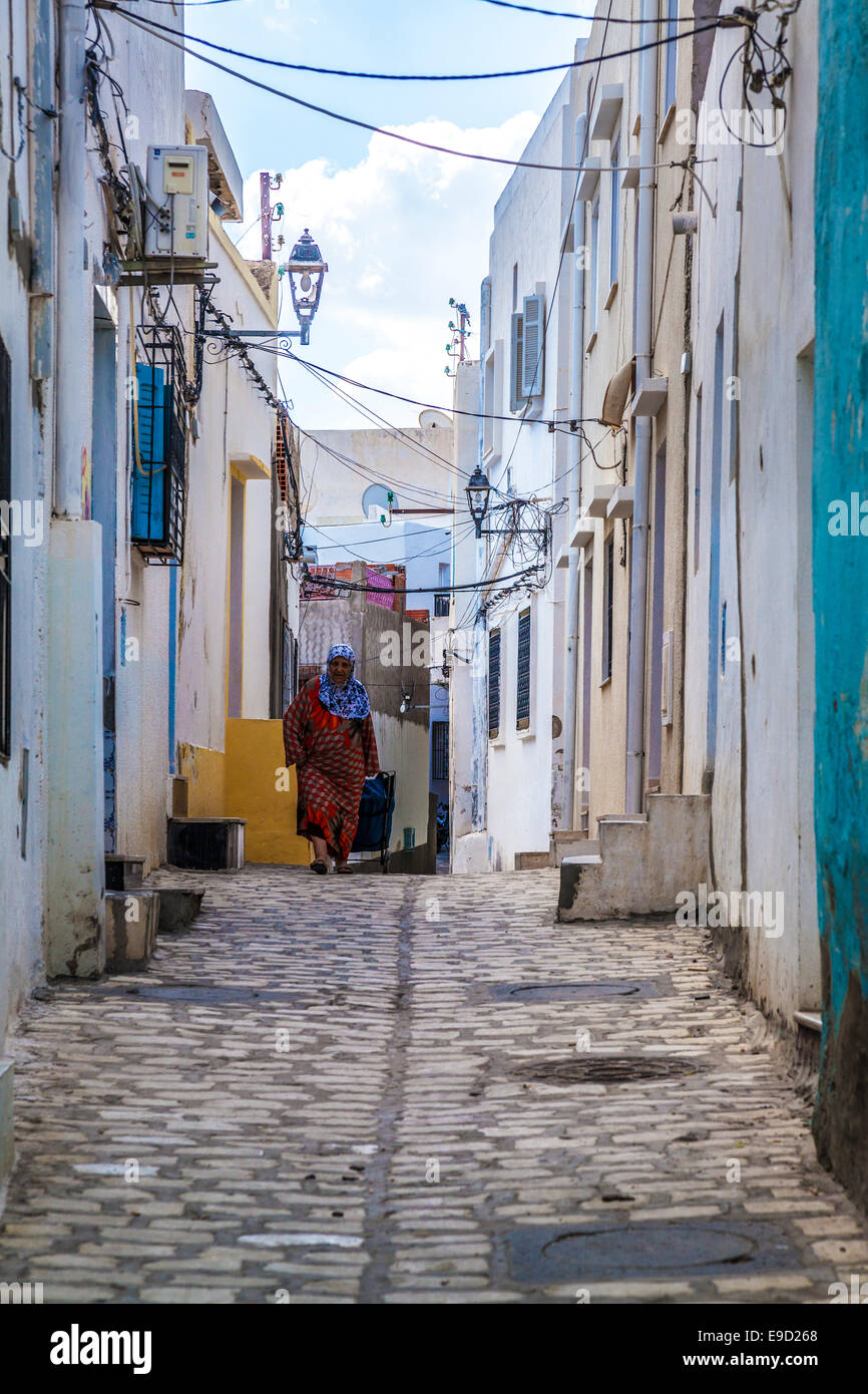 Personnes âgées femme arabe promenades le long d'une petite rue pavées étroites dans la médina de Sousse, Tunisie. Banque D'Images