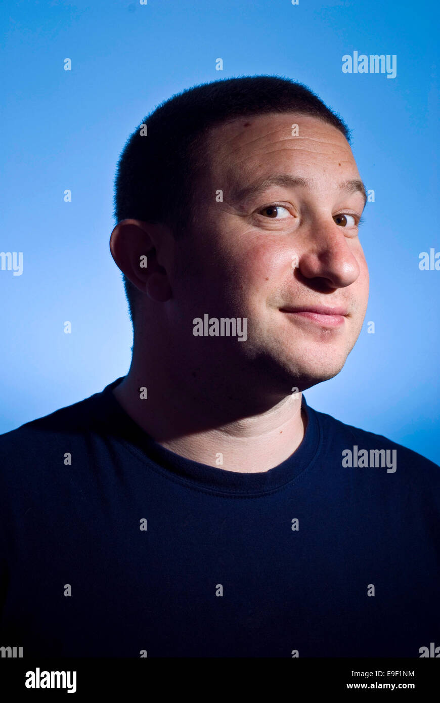 Un petit homme avec un léger sourire et cheveux courts sourit à la caméra dans ce studio portrait avec un fond bleu Banque D'Images
