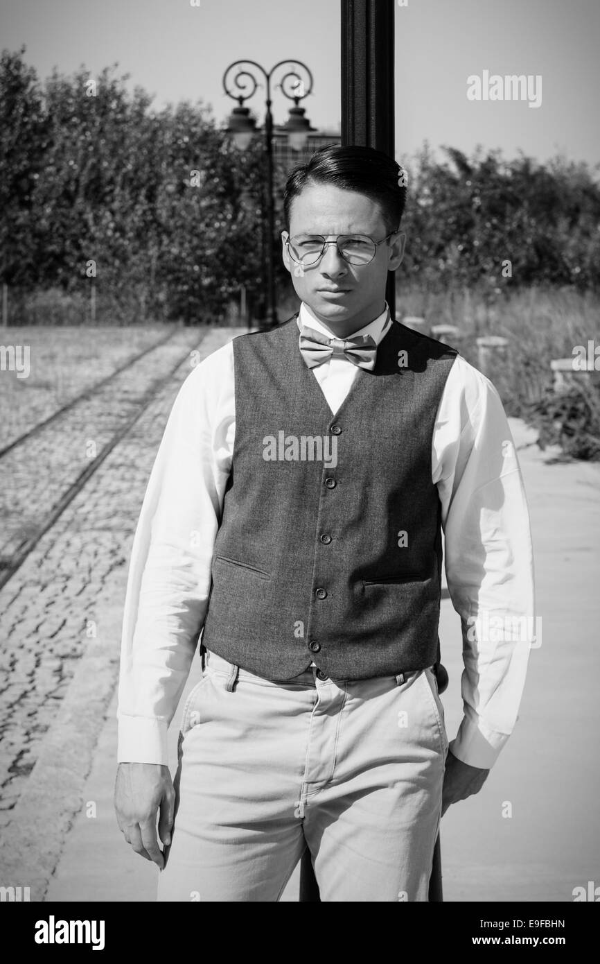 L'homme à veste et bowtie comité permanent par le chemin de fer appuyé contre lampadaire en vieille ville vintage en noir et blanc Banque D'Images