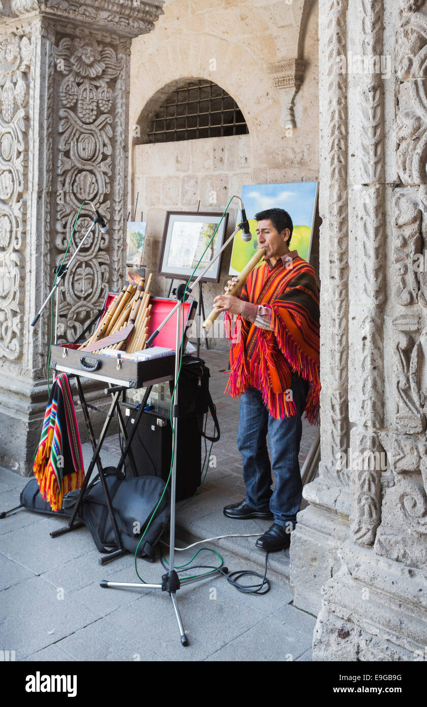 Musicien local jouant en bus des touristes jouant une flûte andine dans le cloître de l'ancienne église jésuite, Iglesia de la Compania, Arequipa, Pérou Banque D'Images