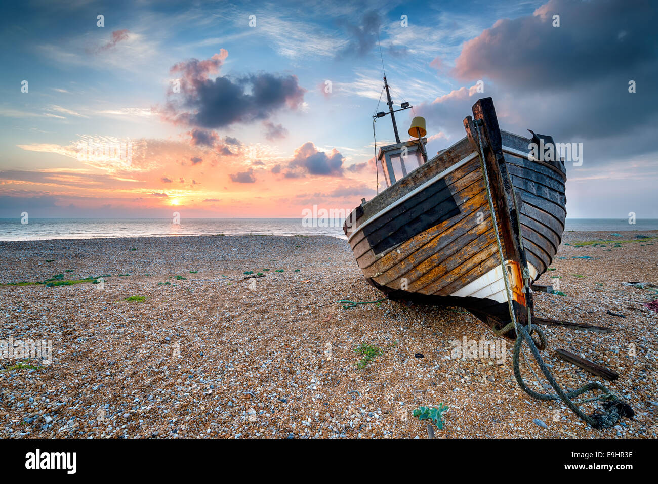Beau lever de soleil sur un vieux bateau de pêche en bois sur une plage de galets Banque D'Images