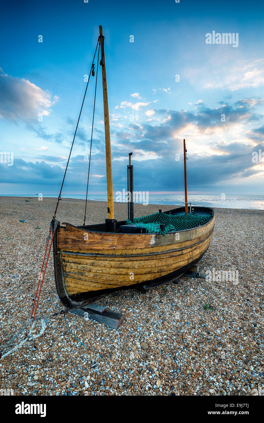 Un petit voilier en bois sur une plage de galets au lever du soleil Banque D'Images