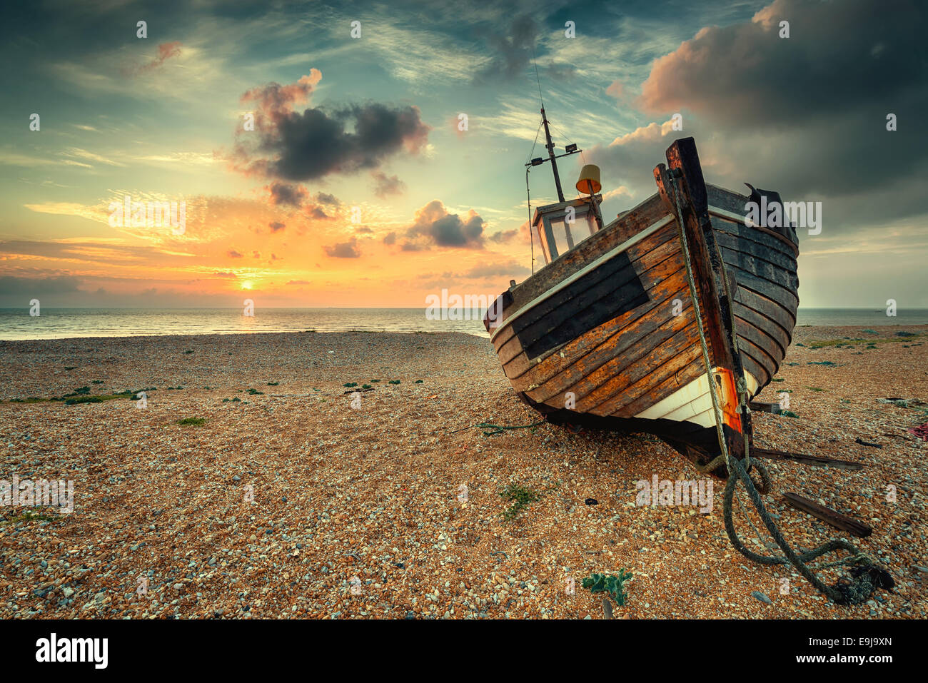 Beau lever de soleil sur un vieux bateau de pêche en bois sur une plage de galets Banque D'Images