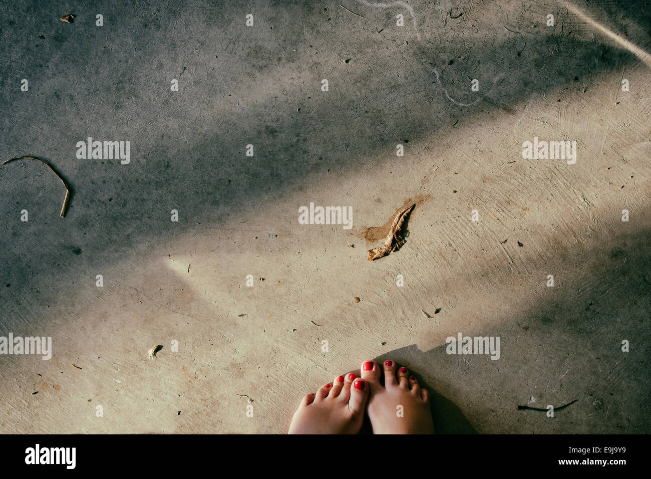 POV shot de 2 pieds avec des ongles rouge debout sur un plancher de ciment sale. Banque D'Images