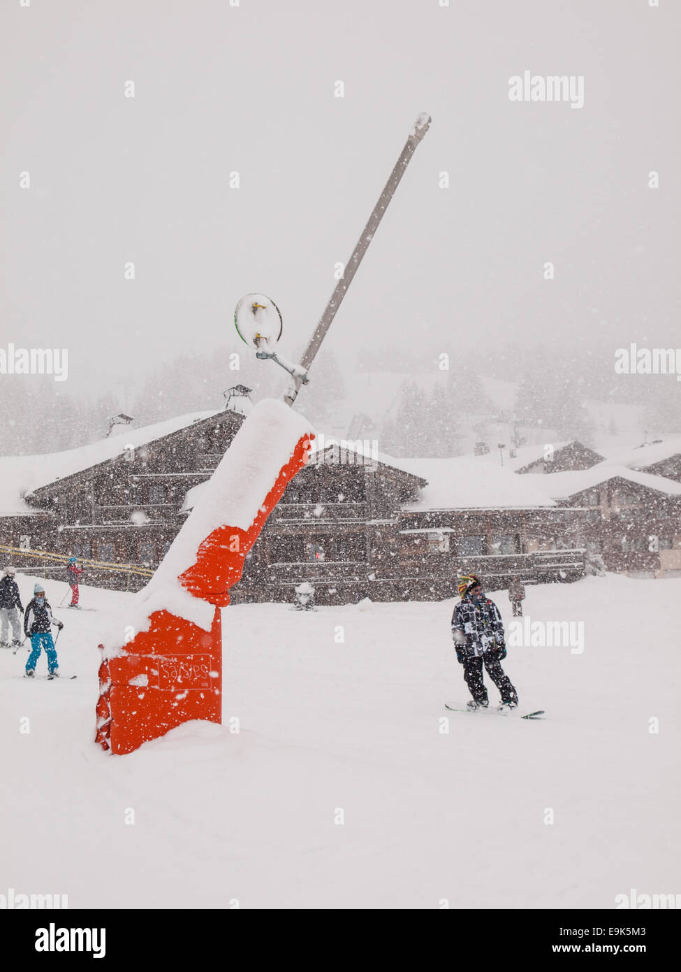 Canon à neige à côté d'une piste à de lourdes chutes de neige dans les Alpes françaises avec les skieurs et snowboarders derrière Banque D'Images