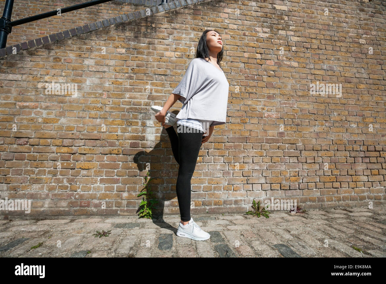 Longueur totale de jeunes fit woman stretching against brick wall Banque D'Images
